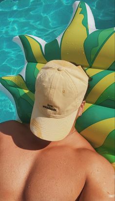 a man wearing a hat sitting next to a swimming pool with inflatable rafts