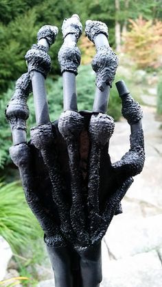 a hand made out of black clay sitting on top of a wooden table in front of some trees