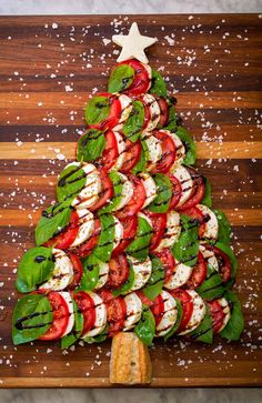 a christmas tree made out of tomatoes and mozzarella on a wooden cutting board