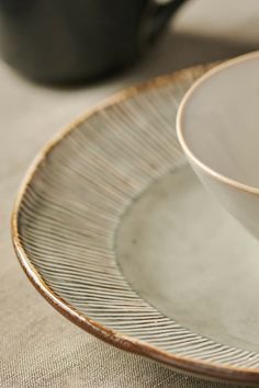 an empty white bowl sitting on top of a plate next to a black coffee cup