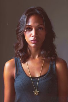 a beautiful young woman wearing a necklace with a cross on it's neck and looking at the camera