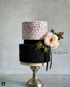 a three tiered cake decorated with flowers and leaves on a silver stand against a gray background