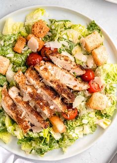 a white plate topped with lettuce and chicken next to bread croutons