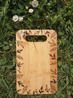 a cutting board sitting in the grass next to daisies