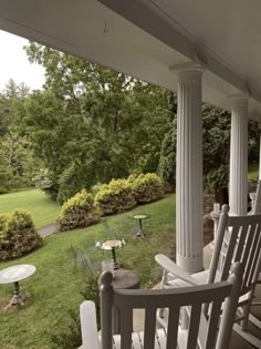 a rocking chair sitting on the front porch of a house with trees in the background