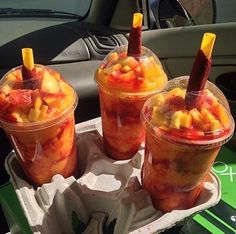 three plastic cups filled with fruit sitting on top of a paper tray in front of a car