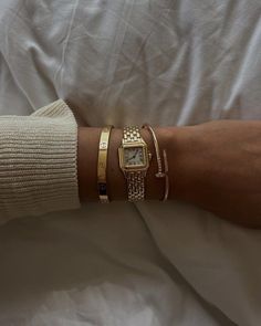 a woman's arm with three bracelets and a gold watch on her wrist