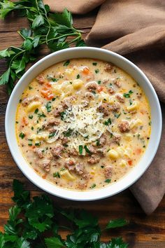 a bowl of soup with meat, cheese and parsley in it on a wooden table