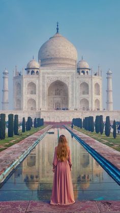 a woman standing in front of the tajwa mosque, with her reflection in the water