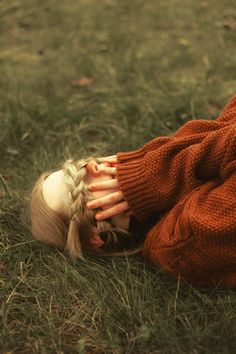 a woman laying in the grass with her hands on her face and hair tied back