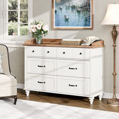 a white dresser sitting in a living room next to a lamp