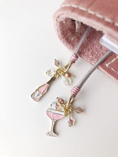 two charms are attached to a pink pouch on a white surface with a book in the background