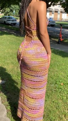 a woman in a crocheted dress is standing on the grass with her back to the camera