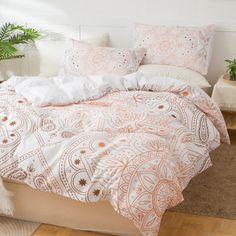 a bed with white and orange comforters in a room next to a potted plant