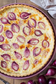 an onion and cheese quiche in a purple dish next to red onions on a wooden table