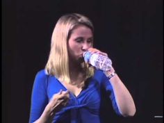 a woman drinking from a water bottle while standing in front of a black background with her hands on her hips