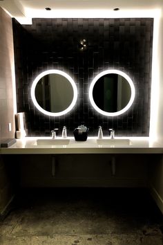 a bathroom with two round mirrors above the sinks and lights on the wall behind it