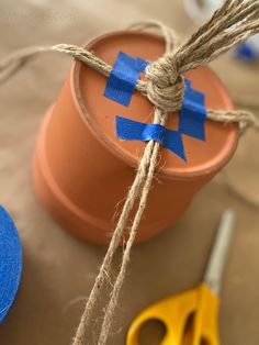 some twine is tied to a pot with blue tape and scissors on the table