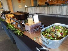 a buffet table with food and drinks on it, including salad in a pan next to a serving dish