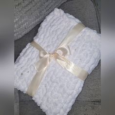 a white blanket wrapped in gold ribbon on top of a gray couch next to a pillow