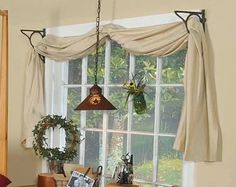 a living room filled with furniture next to a window covered in curtains and hanging plants