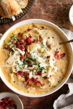 a bowl of soup with cheese and bacon in it next to bread on the side