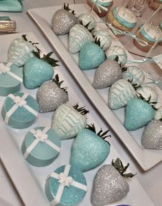 some blue and silver strawberries are on a white plate with other desserts in the background