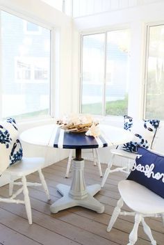 a white table with blue and white pillows on it next to two chairs in front of a window