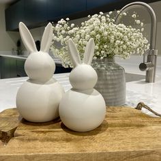 two white ceramic rabbits sitting on top of a wooden cutting board