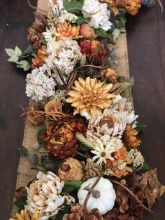 an arrangement of flowers and leaves on a long table runner with burlap ribbon