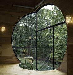 a chair sitting in front of a large round window with trees behind it and a forest outside the window