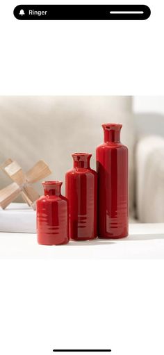 three red vases sitting on top of a white table next to a wooden cross