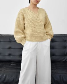 a woman standing in front of a black couch wearing white pants and a yellow sweater