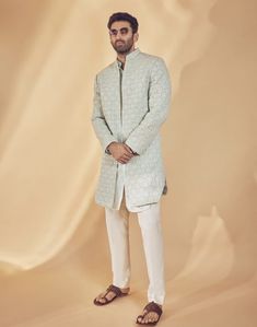 a man standing in front of a beige backdrop wearing a white sherve coat