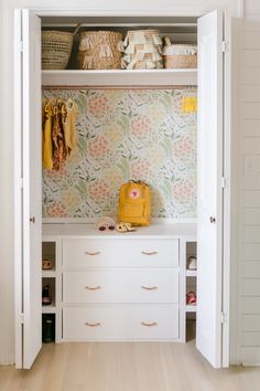 an open closet with white drawers and wallpaper