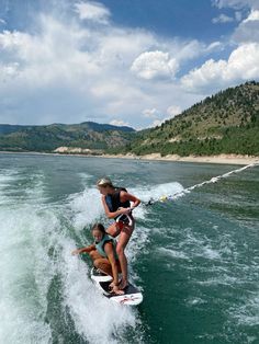 two women riding on the back of a surfboard while being pulled by a boat