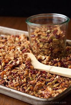 a wooden spoon sitting on top of a pan filled with granola next to a jar of nuts