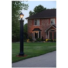 a lamp post in front of a brick house with grass and flowers on the lawn