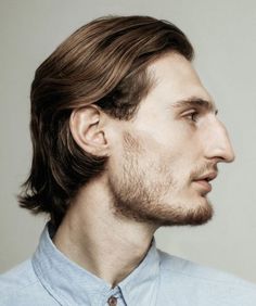 a man with long hair and a beard wearing a blue shirt looking off to the side