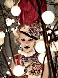 a woman with red hair and feathers on her head is surrounded by christmas lights in the background