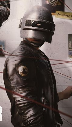 a man in a leather jacket and helmet standing next to a wall with pictures on it