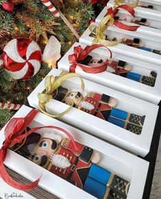 christmas ornaments are lined up on long white trays in front of a decorated christmas tree