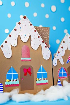 two gingerbread houses made out of cardboard and decorated with paper snow on the ground