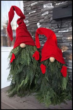 two red hats sitting on top of green plants in front of a brick wall and fireplace