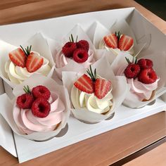 small cupcakes with strawberries and cream frosting in paper wrappers on a table