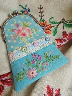 an embroidered purse sitting on top of a white cloth covered tablecloth with floral designs