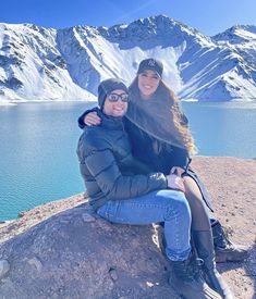 a man and woman sitting on top of a rock next to a body of water