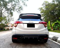 the rear end of a white car parked in a parking lot next to some trees