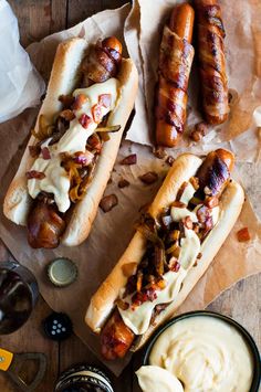 two hot dogs on buns with toppings next to dipping sauce