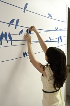 a woman writing on a wall with birds drawn on it and stringing them together